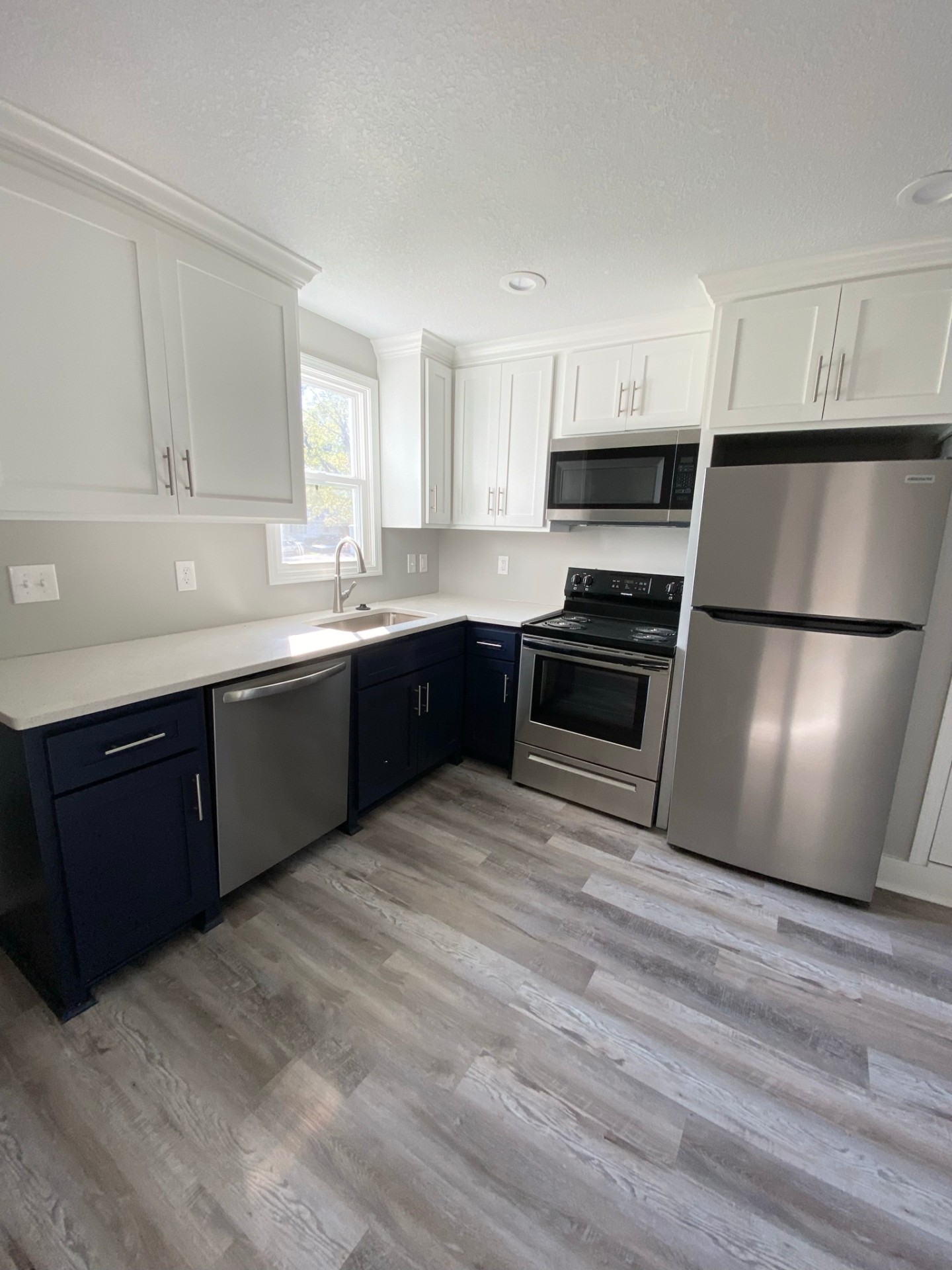 Finished two-tone kitchen with white shaker uppers, navy base cabinets, quartz counters and stainless appliances